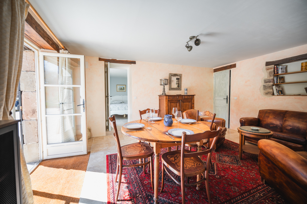 View of the common room of the L’Heure Exquise rural lodge, combining a warm living room with leather armchairs, a wooden dining room and abundant natural light.