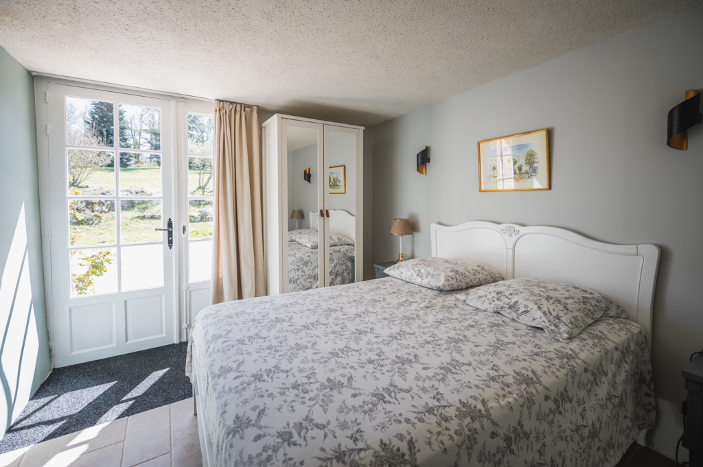 Bright interior of the Crépuscule bedroom with a double bed, a white wardrobe and a clear view of the green garden.