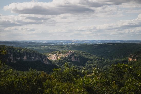 Photo panoramique de Bruniquel, village médiéval perché, entouré de collines verdoyantes et de falaises spectaculaires.