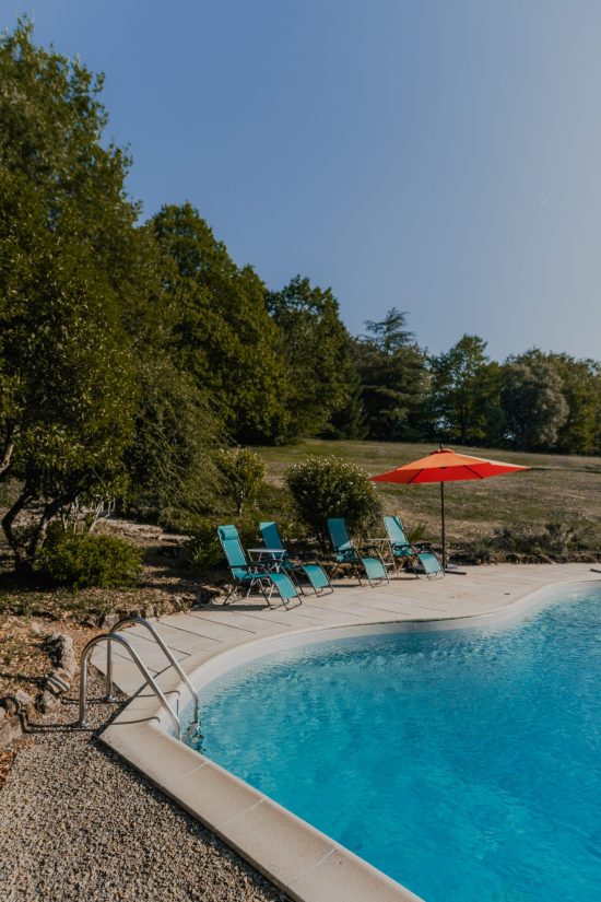 Photo of the swimming pool at the L’Heure Exquise lodge with deck chairs on the edge of the undergrowth, lit by the sun.