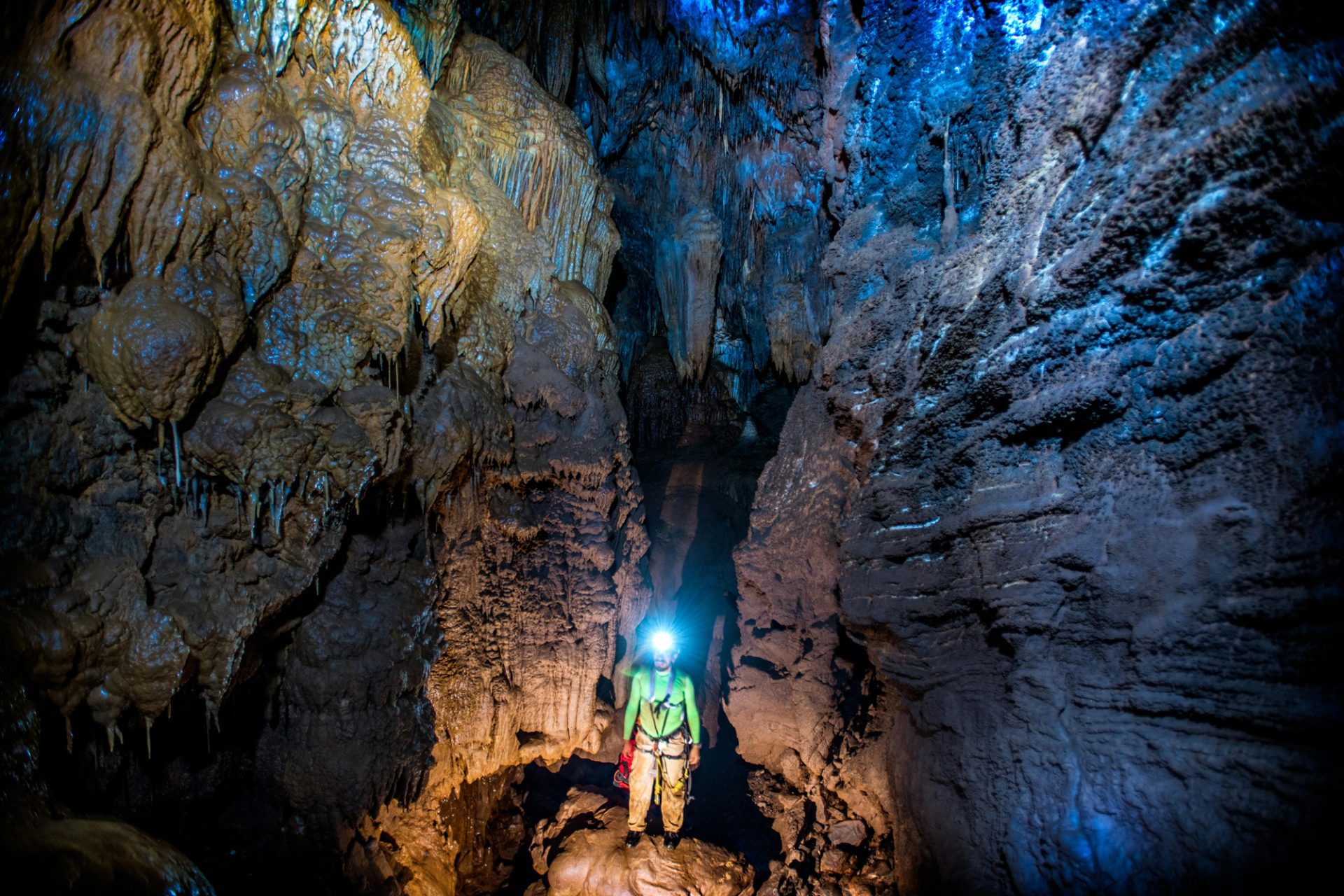 Photo d’un homme équipé pour la spéléologie, explorant une grotte avec un casque et une lampe frontale