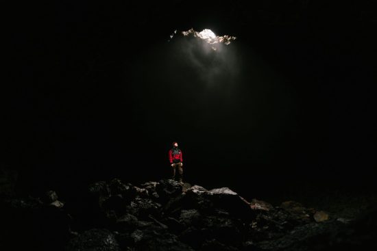 Photo d’une personne debout dans une grotte, éclairée par un puits de lumière naturel traversant la roche