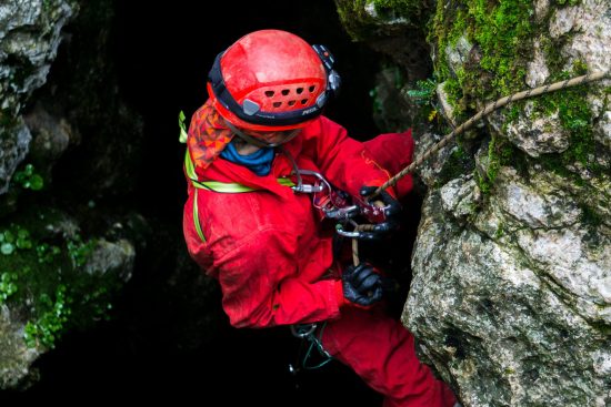 Photo d’une personne équipée pour la spéléologie, descendant en rappel le long d’une paroi rocheuse dans une grotte