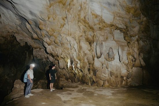 Photo de deux touristes équipés de casques et de lampes frontales, explorant une grotte aux formations rocheuses spectaculaires