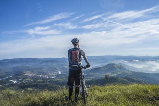 Photo d’un cycliste en VTT arrêté au sommet d’un sentier, contemplant un paysage naturel à couper le souffle