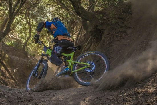 Photo of a cyclist practicing mountain biking on a wooded trail, surrounded by trees and greenery