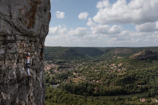 Photo de deux personnes équipées pour la via ferrata, progressant sur une falaise avec vue sur Saint-Antonin-Noble-Val et la rivière Aveyron