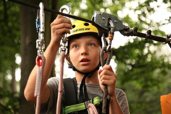 Photo of a child wearing a helmet and harness, attaching himself to the lifeline before starting a via ferrata course