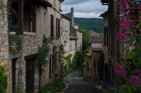 Photo of a street in Bruniquel, lined with stone houses typical of medieval architecture, with a view of the green hills in the background