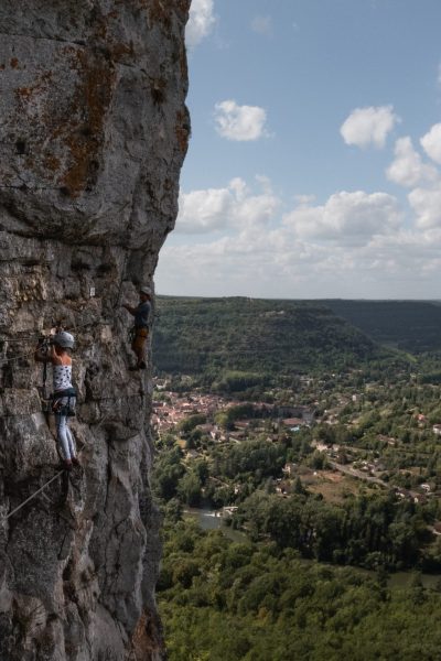 Two climbers ascending a cliff with a panoramic view of Saint-Antonin-Noble-Val and the Aveyron river